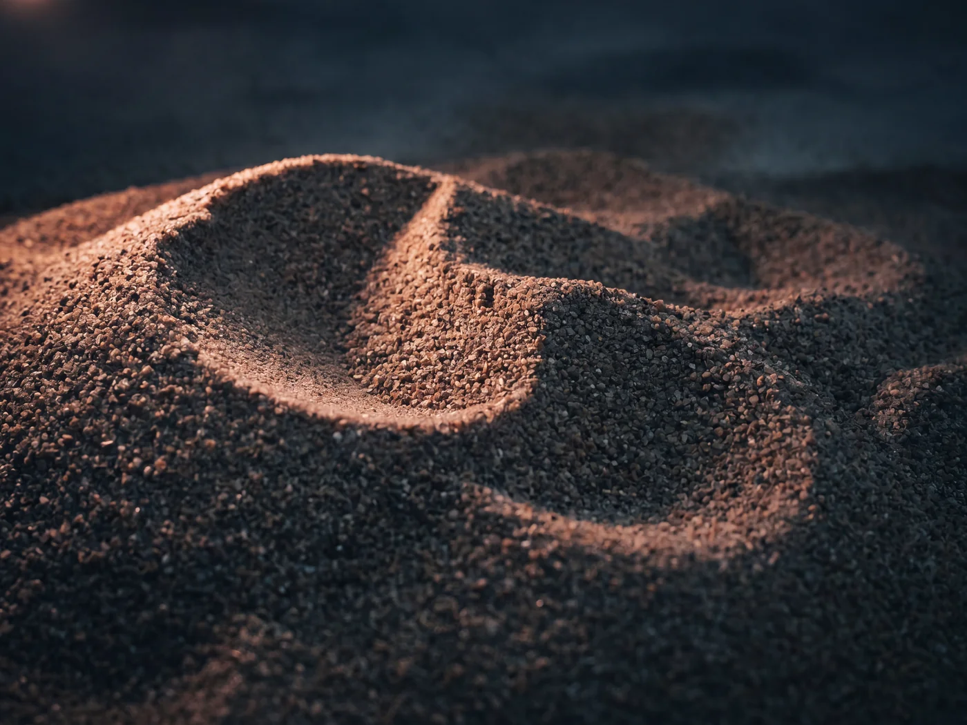 Close up of sharp sand, coarse gritty grains mounded under soft raking light